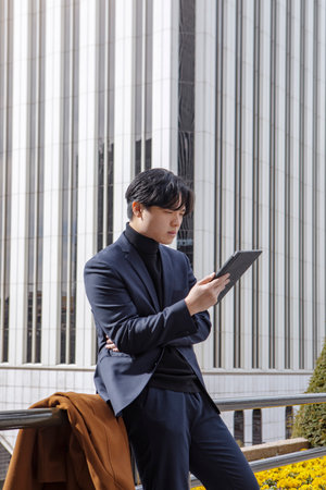 asian man outside the business center, talking on his cell phone, while looking at his tablet. High quality photoの写真素材