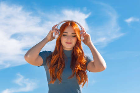 Cute young woman listening to music with wireless headphones and looking down with the sky in the background and copy space. . High quality photoの写真素材