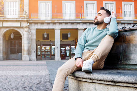 young man sitting on the street listening to music with wireless headphones. High quality photoの写真素材