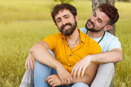 Couple of gay men sitting in the park against a tree. High quality photoの写真素材