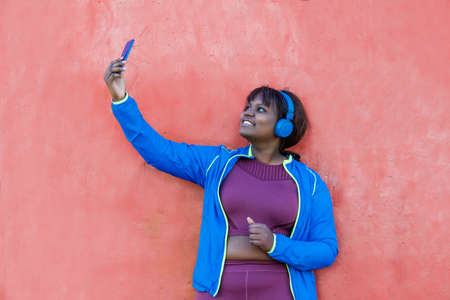 Young black woman, against a colorful wall, looking at her cell phone taking a selfie. High quality photoの写真素材