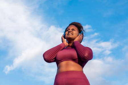 African woman listening to music through headphones, with blue sky in the background. High quality photoの写真素材