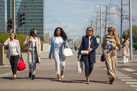 group of five women of different ages talking while walking on the street in the modern city happy and smiling. High quality photosの写真素材