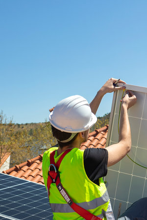 Man technician mounting photovoltaic solar modules on roof of house. Engineer in helmet installing solar panel system outdoors. Concept of alternative and renewable energy. High quality photosの写真素材