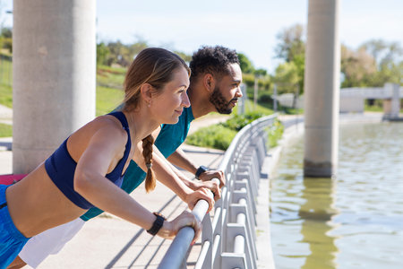multi-ethnic couple in sportswear perform push-up exercise on a metal bar outdoors in an urban park. High quality photosの写真素材