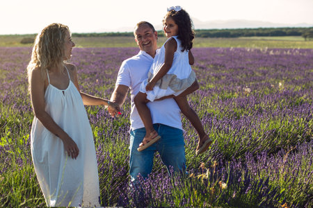 Happy Caucasian Family in Purple Lavender Field. Parent Couple and Little Girl Enjoy Walking Blooming Meadow on Summer Day.の写真素材