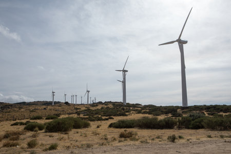 Majestic wind turbines rise against a backdrop of fluffy clouds in a picturesque landscape. The sun...