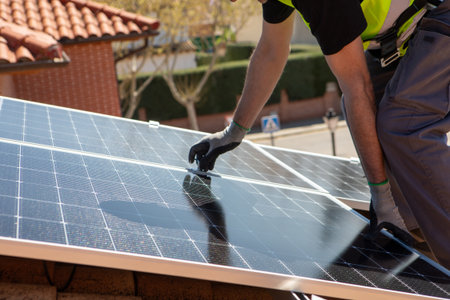 A worker carefully attaches solar panels to a rooftop as part of an energy-efficient upgrade. The bright sunlight highlights the project in an urban setting.の写真素材