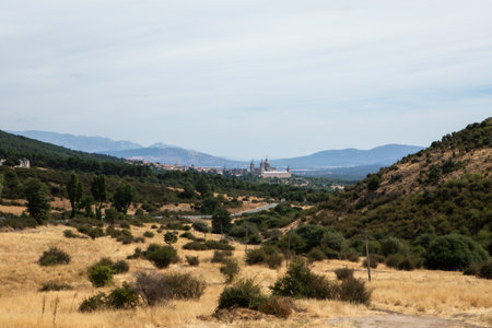 A vast landscape showcases hills, dry grasslands, and a distant town featuring notable architecture. The clear sky enhances the serene atmosphere of this rural area.の写真素材