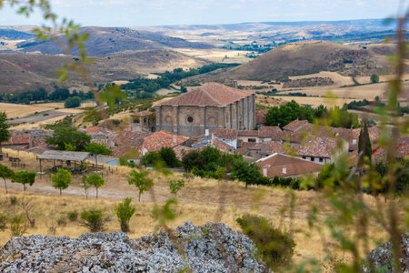Overlooking Atienza in Guadalajara, this viewpoint reveals the town's historic buildings nestled in a vast rural landscape, framed by rolling hills and greenery under a cloudy sky.の写真素材
