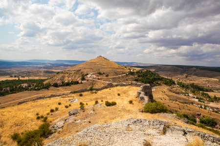 A picturesque view of the rolling hills surrounding Atienza, Guadalajara, Spain shows ancient ruins and grassy terrain under a bright sky, perfect for outdoor exploration and photography.の写真素材