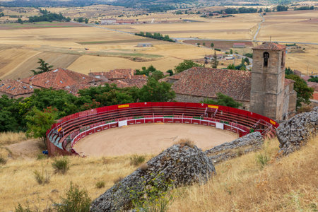A bullring sits prominently in Atienza, Guadalajara, Spain, with a backdrop of arid fields and rolling hills. The rustic village offers a glimpse into traditional Spanish culture.の写真素材