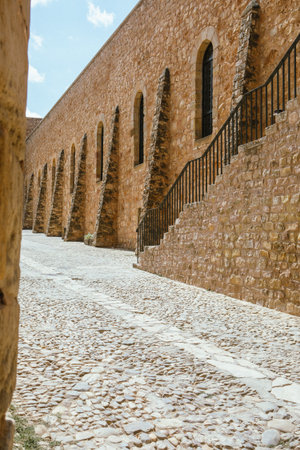 Visitors stroll along a cobblestone path surrounded by ancient stone walls and stairs of a historical fort, enjoying the clear blue sky and architectural beauty.の写真素材