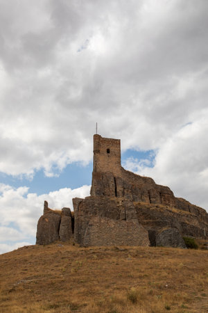 Atienza castle stands majestically atop a rocky hill in Guadalajara, Spain, showcasing its story past against a backdrop of dramatic clouds. The landscape is dry and rugged.の写真素材