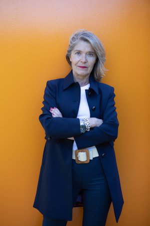 A confident woman stands against a vibrant orange wall. She appears self-assured with her arms crossed and a friendly expression on her face.の写真素材