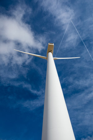 Marvel at the impressive height of wind turbines stretching towards the azure sky. Feel the breeze while embracing the harmony of nature and renewable energy in a peaceful setting.の写真素材
