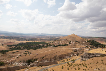A picturesque view of the rolling hills surrounding Atienza, Guadalajara, Spain shows ancient ruins and grassy terrain under a bright sky, perfect for outdoor exploration and photography.の写真素材