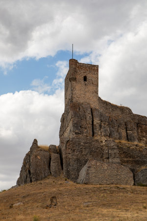 Atienza castle stands majestically atop a rocky hill in Guadalajara, Spain, showcasing its story past against a backdrop of dramatic clouds. The landscape is dry and rugged.の写真素材