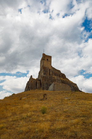 Atienza castle stands majestically atop a rocky hill in Guadalajara, Spain, showcasing its story past against a backdrop of dramatic clouds. The landscape is dry and rugged.の写真素材