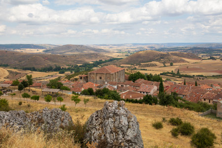 Overlooking Atienza in Guadalajara, this viewpoint reveals the town's historic buildings nestled in a vast rural landscape, framed by rolling hills and greenery under a cloudy sky.の写真素材