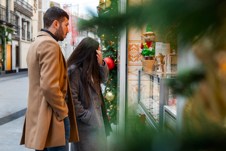 A couple stands close together, gazing in wonder at a display of holiday sweets. The charming street is adorned with festive decorations, creating a warm atmosphere.の写真素材