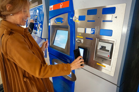 A woman in a stylish brown coat stands at a bright blue ticket vending machine. She scans her phone...