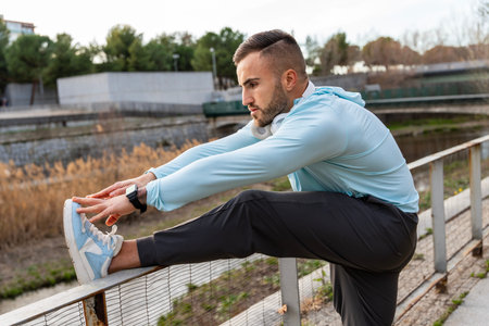 A young man performs a deep stretch by a serene river, embracing the morning calm. The gentle light...