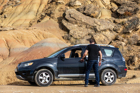 A traveler steps out of a vehicle to admire the vibrant, unique rock formations of Bardenas Reales...