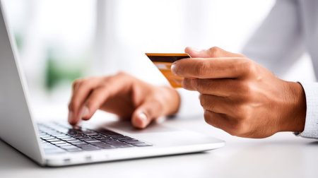 In a sunlit room, a person focuses on their laptop screen while holding a credit card in their right hand. The atmosphere feels vibrant and modern, perfect for online shopping.の素材