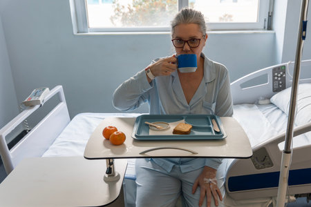 Patient enjoys a quiet moment in a hospital room after lumbar arthrodesis surgery. A tray holds simple breakfast essentials as recovery begins and hope builds.の写真素材