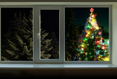 Christmas tree decorated with bright colored lights is outside the windowの写真素材