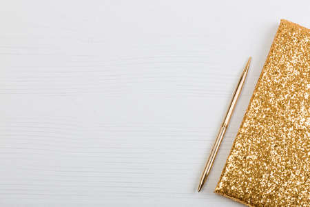 Golden sparkling notebook for recording closeup and a pen lying on a white table.