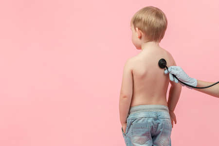 Pediatrician doctor listens with a stethostop or phonendoscope to a child of a boy with red hair on...