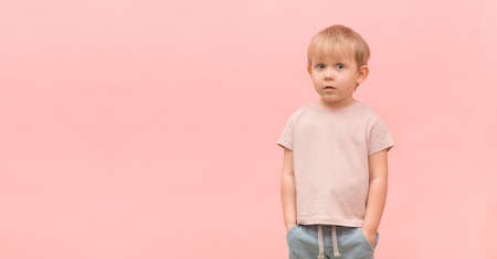 Portrait of a child of a 3 years old blond boy looking surprised at the camera on a pink background with place for text. Banner concept for website heading or flyer advertising.の写真素材