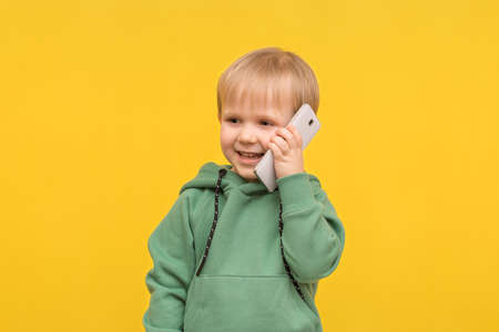 Child boy blond talking on the phone smartphone on a yellow spring background. Concept for articles about modern childhood, children's communication, the impact of technology on development.の写真素材