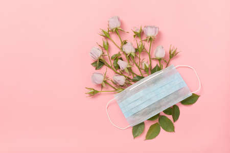 Medical respiratory protective face mask and delicate roses on a pink background, of coronavirus and covid-19. The concept of spring, positive thoughts and romance after an illness, life goes on.の写真素材