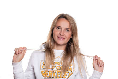 Blonde beautiful girl with long hair in a sweatshirt on a white background smiles and looks into the...