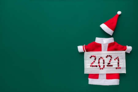 Christmas and new year symbol, santa claus costume in coronavirus medical protective mask 2021. New reality concept, festive flat lay postcard with place for text on green background.の写真素材