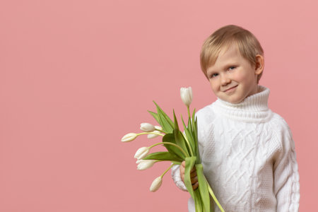 Child kid boy with flowers white tulips in knitted sweater on pink solid background with copy space. Concept for Valentine day, woman day March 8 and mother day. Postcard mockup with space for text.の写真素材