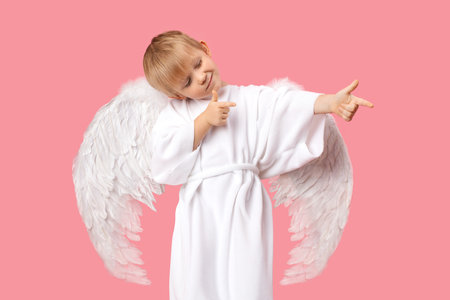 Angel Cherub child boy with large white wings is aiming at man to make him fall in love. Studio shot postcard on pastel pink background. Concept for Valentine Day 14 February.の写真素材