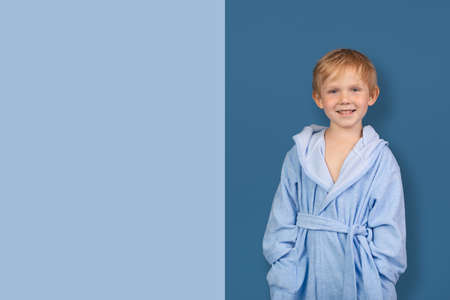 Mockup template caucasian child laugh smile in bathrobe for sauna. Advertising concept for children clothing store and spa, swimming pool. Studio shot with blue bar with copy space text.の写真素材