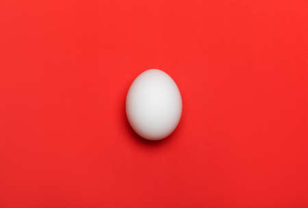White egg on bright red background. Close-up macro flatlay, flat lay with texture. Food and Easter concept.の写真素材