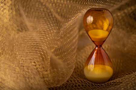 Brown hourglass glass clock on gold honeycomb lattice background. Concept of transience of expiring...