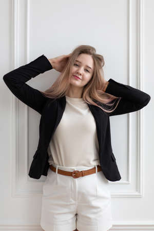 Beautiful young Caucasian woman in casual office clothes standing and touching her hair, posing,...