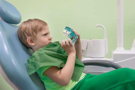 Boy man child at dentist in chair look at white teeth. Curious, serious look. Oral health and hygiene concept, dental clinic.の写真素材