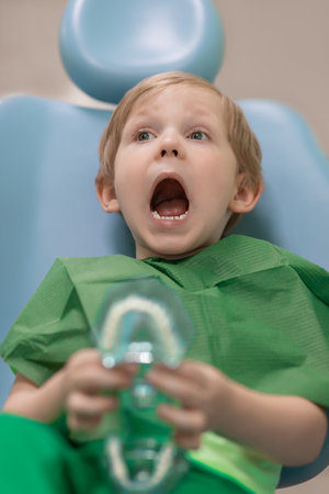 Child kid with his mouth wide open is waiting for doctor examination in dental chair at dentist....