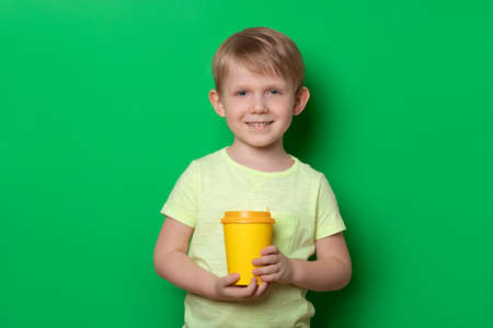 Caucasian man hold disposable cup with drink of coffee or tea and look into camera on plain green background. Studio shot concept.の写真素材
