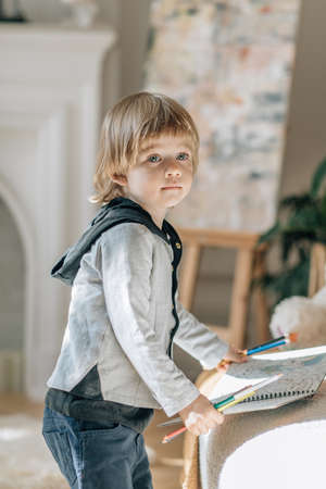 Child toddler blond kid stand draw with pencils inside house, vertical shot.
