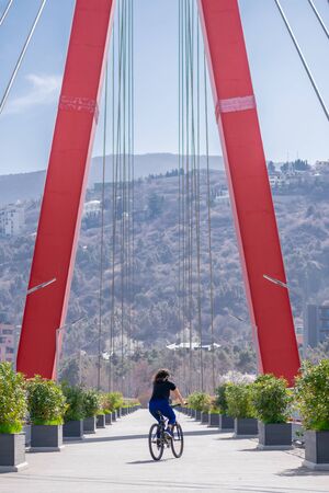 Female person without helmet cycling through red Maglivi bridge in Tbilisi suburbs. Sakartvelo.Georgia.の写真素材
