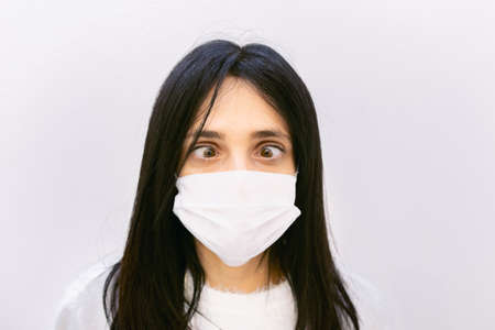 Youn caucasian woman shows crazy eye look down to whte face mask. concept of sickness and human...